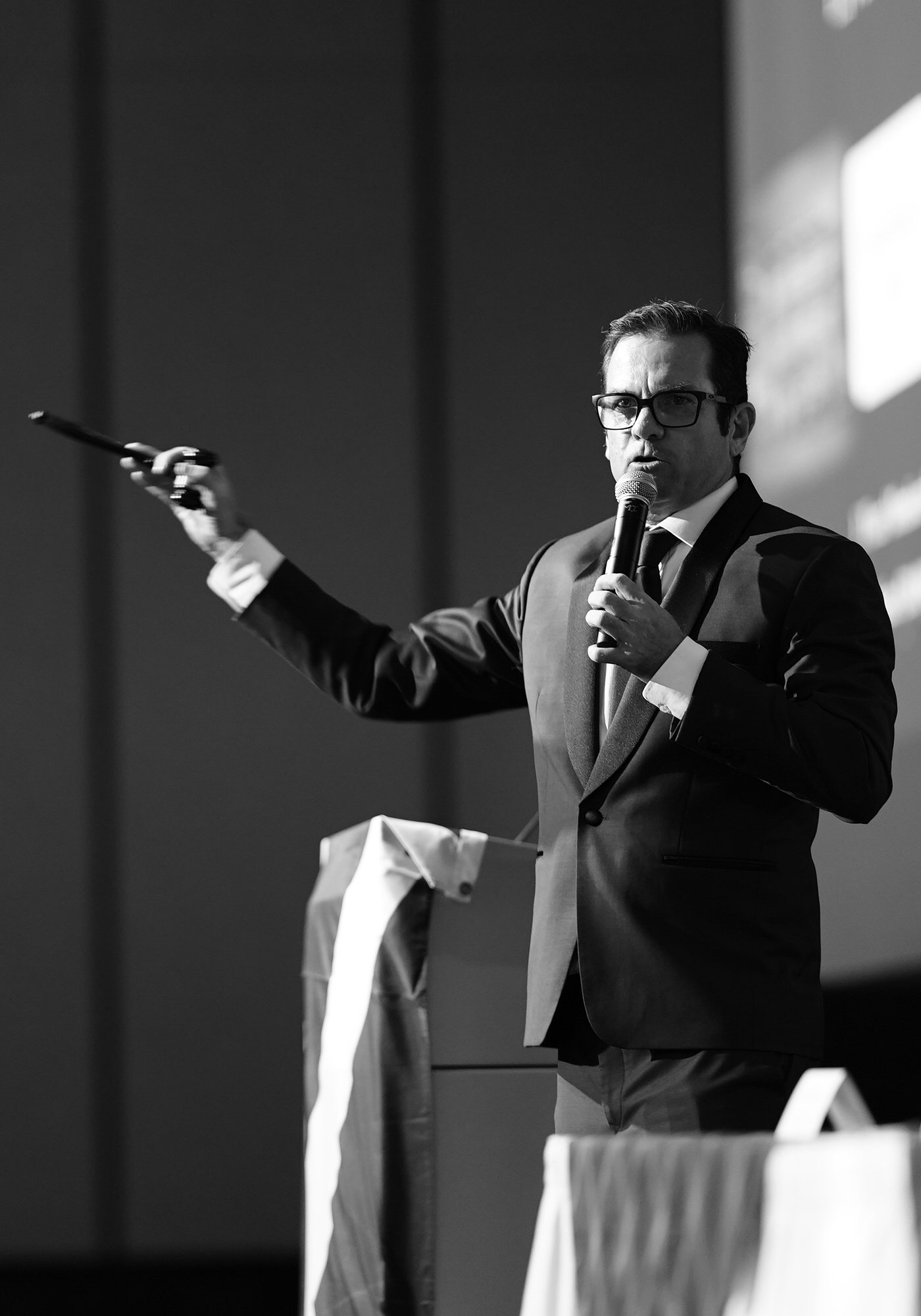 Shaun McEwan on stage with a microphone, gesturing to the audience
